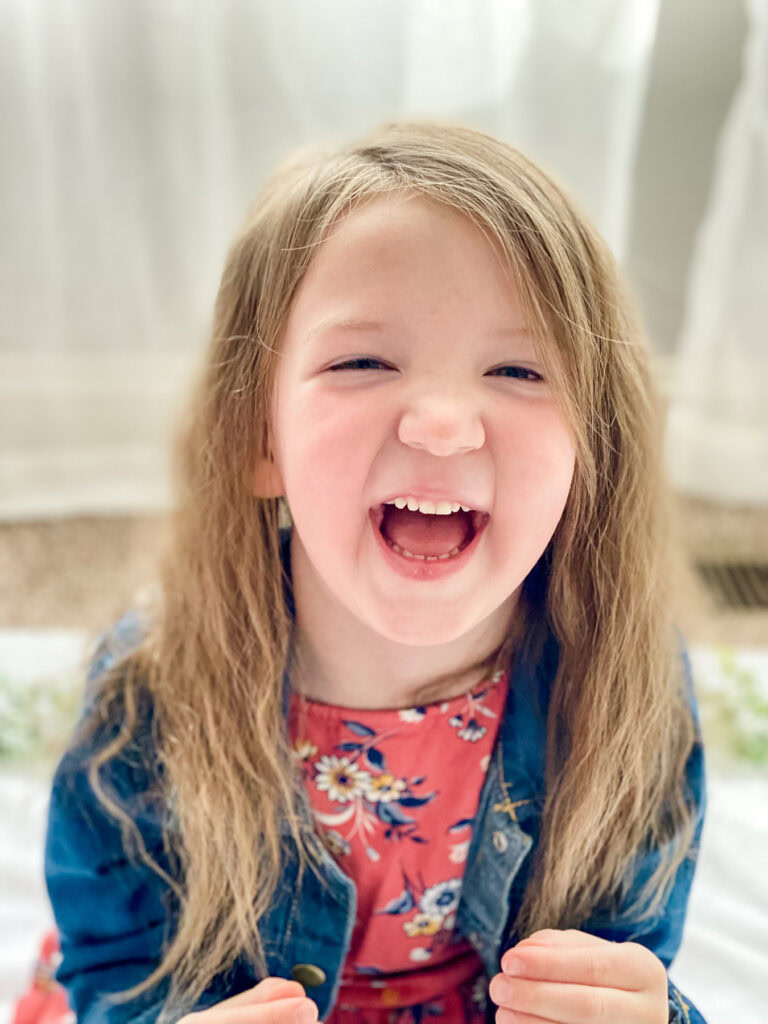 A little girl laughing while sitting on a bed.